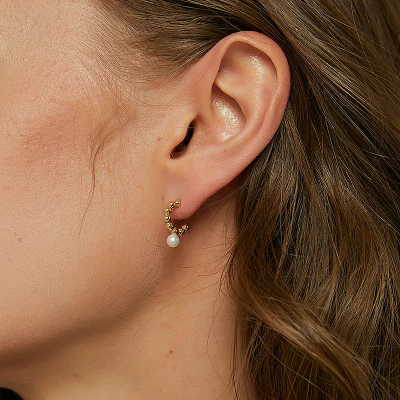 Boucles d’oreilles dorées demi-créoles pour femme en plaqué or, ornées d’une perle blanche nacrée suspendue. Bijou sculptural et raffiné au design moderne et féminin, parfait pour un style chic et contemporain