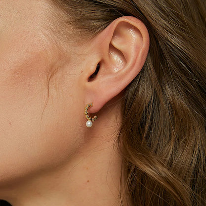 Boucles d’oreilles dorées demi-créoles pour femme en plaqué or, ornées d’une perle blanche nacrée suspendue. Bijou sculptural et raffiné au design moderne et féminin, parfait pour un style chic et contemporain