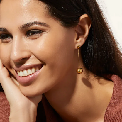 Boucles d’oreilles pendantes dorées longues pour femme en acier inoxydable, avec tige fine et bille suspendue brillante. Bijou chic, minimaliste et contemporain, hypoallergénique et résistant à l’eau, idéal pour un look urbain raffiné