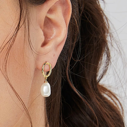 Boucles d’oreilles pendantes dorées pour femme, composées d’un ovale martelé doré et d’une perle blanche baroque suspendue. Bijou au style bohème chic et raffiné, lumineux et féminin, parfait pour sublimer une tenue naturelle ou romantique