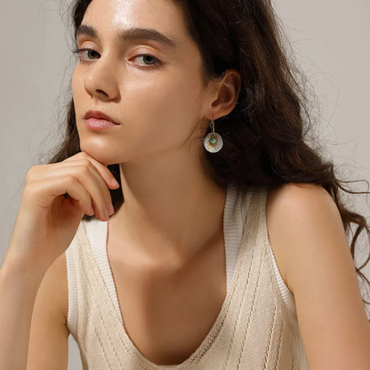 Boucles d’oreilles pendantes dorées en acier inoxydable, disque en nacre naturelle décoré d’un motif soleil et d’un centre turquoise. Bijou bohème chic et lumineux, hypoallergénique et résistant à l’eau