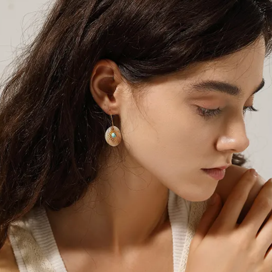 Boucles d’oreilles pendantes dorées en acier inoxydable, disque en nacre naturelle décoré d’un motif soleil et d’un centre turquoise. Bijou bohème chic et lumineux, hypoallergénique et résistant à l’eau