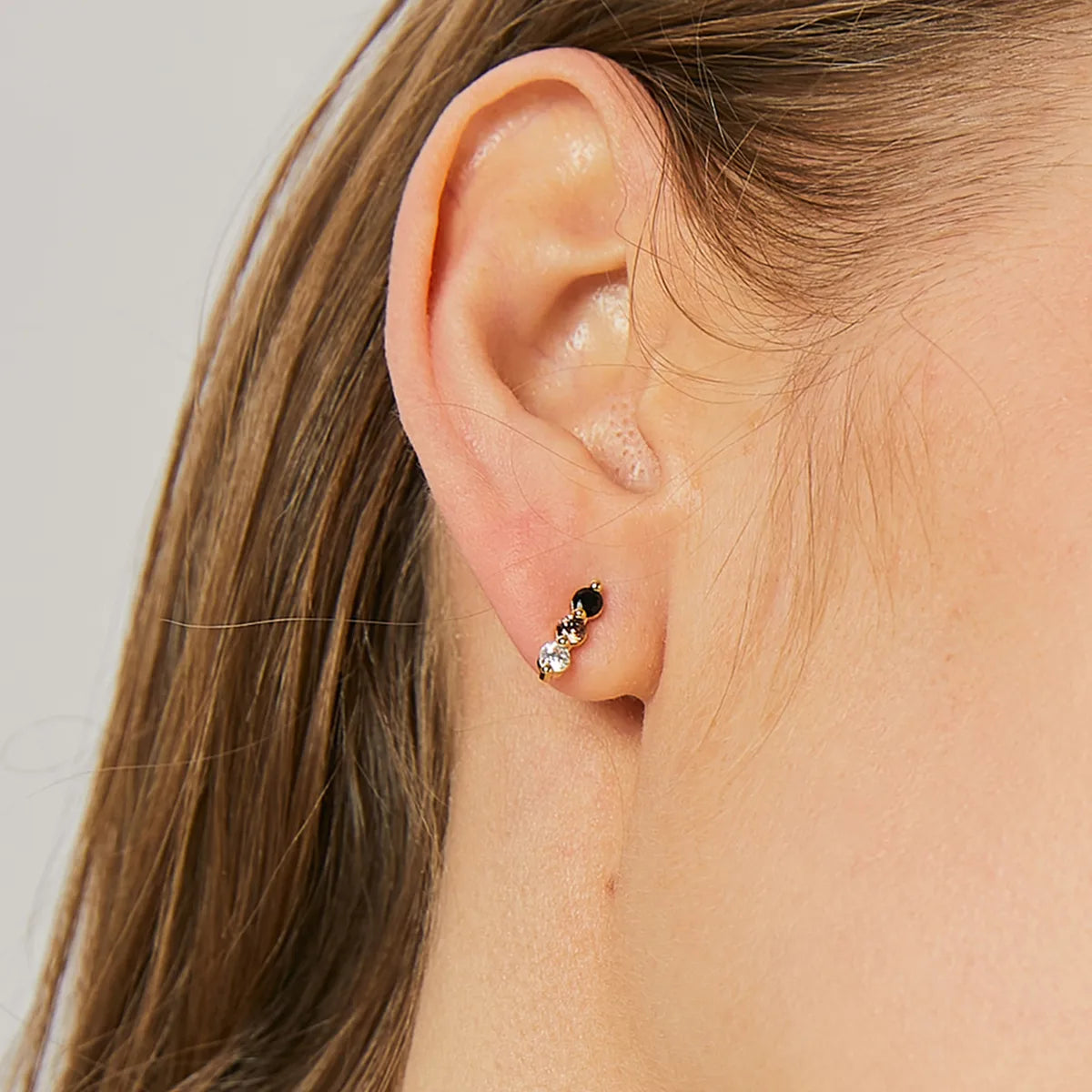Boucles d’oreilles puces dorées pour femme en plaqué or, ornées de trois pierres alignées en dégradé noir, cognac et blanc. Bijou minimaliste et raffiné au design graphique, parfait pour un port quotidien discret ou un look élégant et coloré.