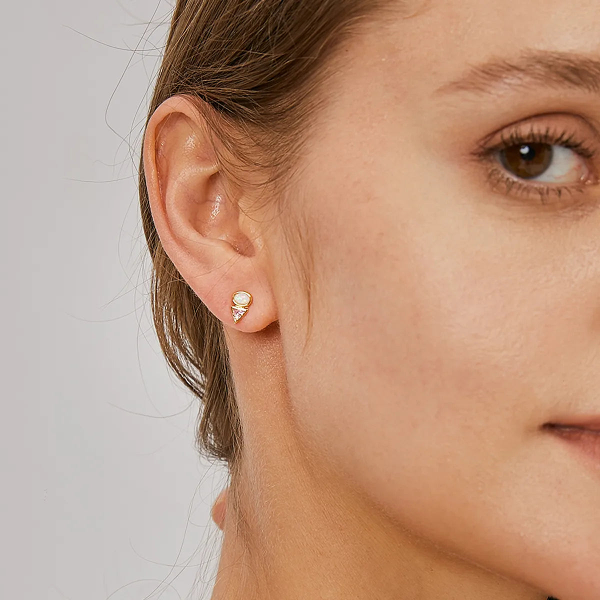 Boucles d’oreilles puces dorées pour femme en plaqué or, associant une opale blanche iridescente et un zircon rose taillé en triangle inversé. Bijou féminin et moderne au design géométrique et lumineux, parfait pour un look chic et contemporain