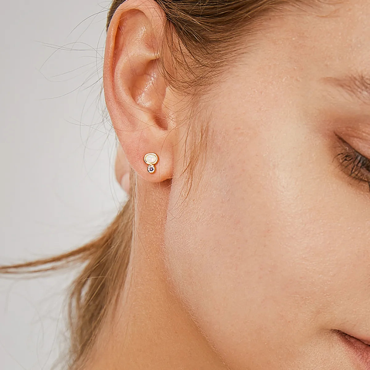 Boucles d’oreilles puces dorées pour femme en plaqué or, ornées d’une opale blanche irisée et d’un zircon violet scintillant. Bijou délicat et contemporain au design minimaliste, idéal pour un port quotidien ou une accumulation élégante