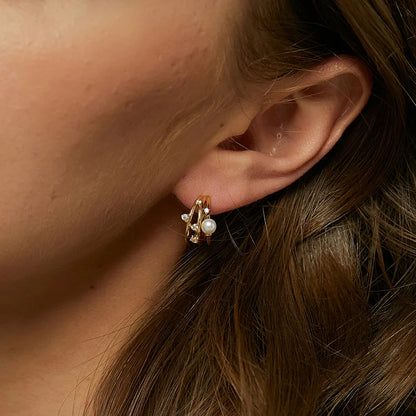 Boucles d’oreilles puces dorées pour femme en plaqué or, composées de deux anneaux entrelacés ornés de zircons scintillants et d’une perle blanche ronde. Bijou chic et raffiné, au design moderne et féminin, idéal pour une tenue habillée ou élégante au quotidien