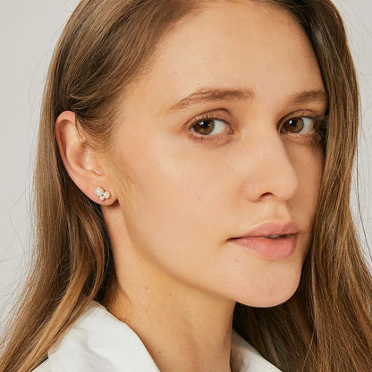 Boucles d’oreilles puces dorées pour femme en plaqué or, ornées de trois perles blanches disposées en grappe minimaliste. Bijou délicat et lumineux au style chic et féminin, parfait pour un look minimaliste ou une accumulation raffinée.