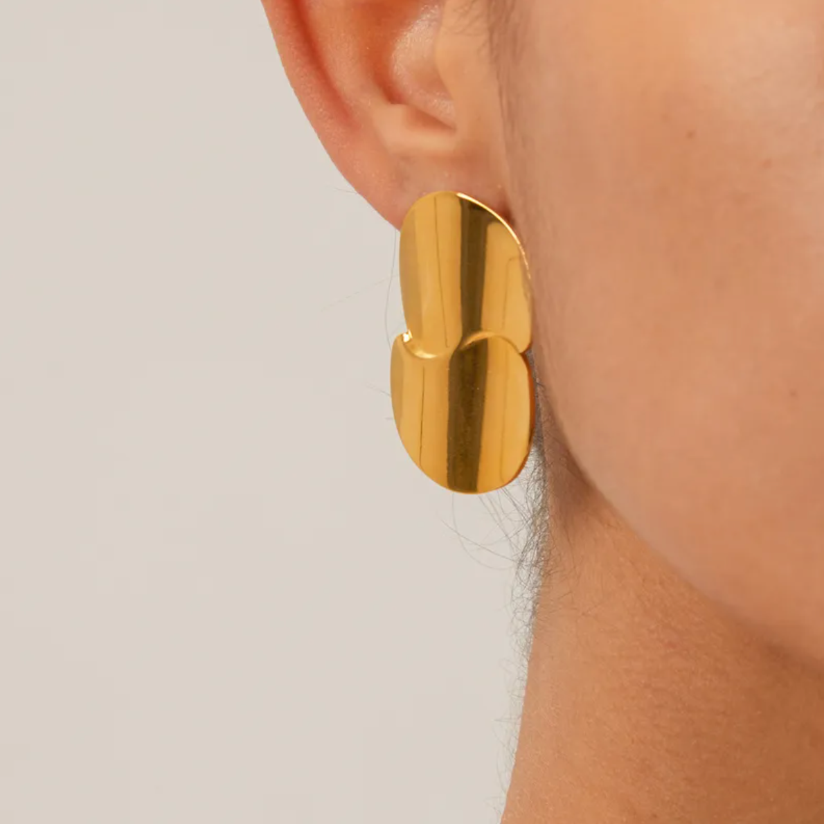 Boucles d’oreilles puces dorées pour femme en acier inoxydable, au design organique et sculptural inspiré de pétales fusionnés. Bijou arty et moderne au fini miroir, résistant à l’eau et hypoallergénique, idéal pour un look élégant ou de cérémonie