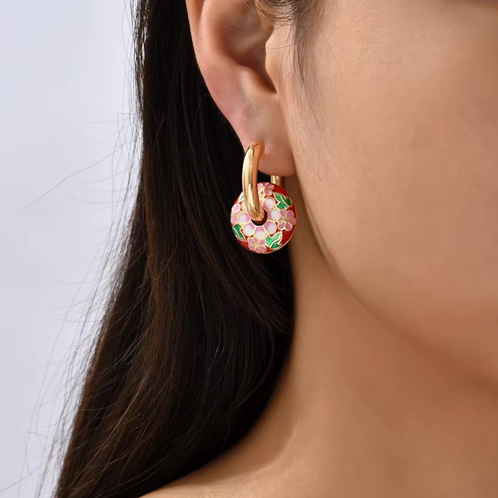 Boucles d’oreilles créoles couleur or avec pendentif rond émaillé motif floral multicolore.