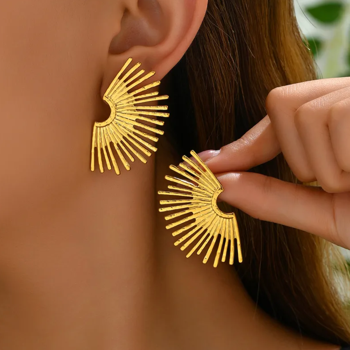 Des boucles d’oreilles puces au design solaire, puissantes et expressives, inspirées d’un éventail de lumière. Leur forme évoque à la fois des ailes déployées et un coucher de soleil stylisé, pour un rendu résolument moderne et sculptural.

Matériau : Acier inoxydable couleur doré, résistant à l’eau, sans ternissure, hypoallergénique.

Dimensions : 44 x 26 mm – format large, affirmé, mais léger (12 g la paire).

Design : Structure en éventail rayonnant, effet martelé subtil qui capte la lumière. Style graph