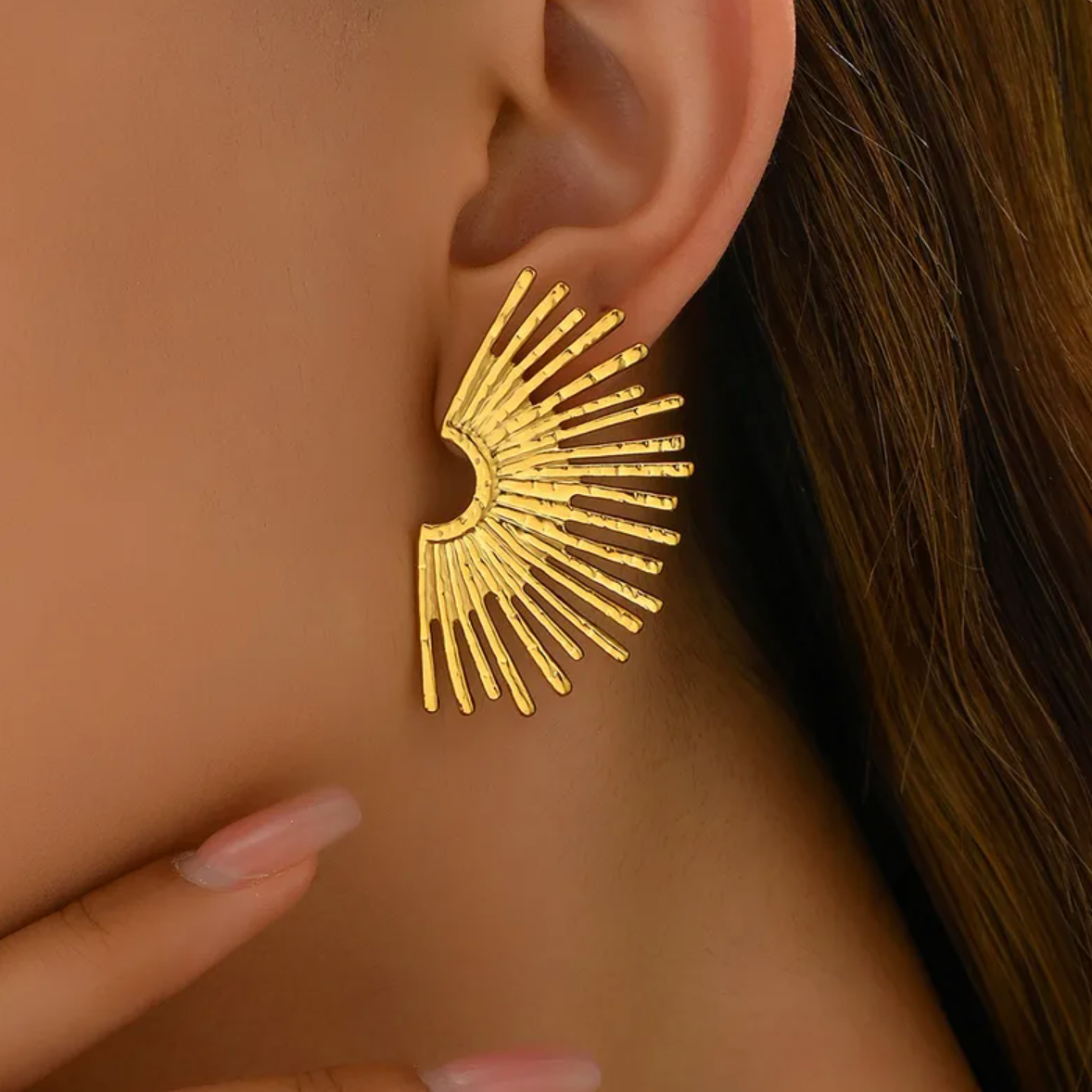 Des boucles d’oreilles puces au design solaire, puissantes et expressives, inspirées d’un éventail de lumière. Leur forme évoque à la fois des ailes déployées et un coucher de soleil stylisé, pour un rendu résolument moderne et sculptural.

Matériau : Acier inoxydable couleur doré, résistant à l’eau, sans ternissure, hypoallergénique.

Dimensions : 44 x 26 mm – format large, affirmé, mais léger (12 g la paire).

Design : Structure en éventail rayonnant, effet martelé subtil qui capte la lumière. Style graph