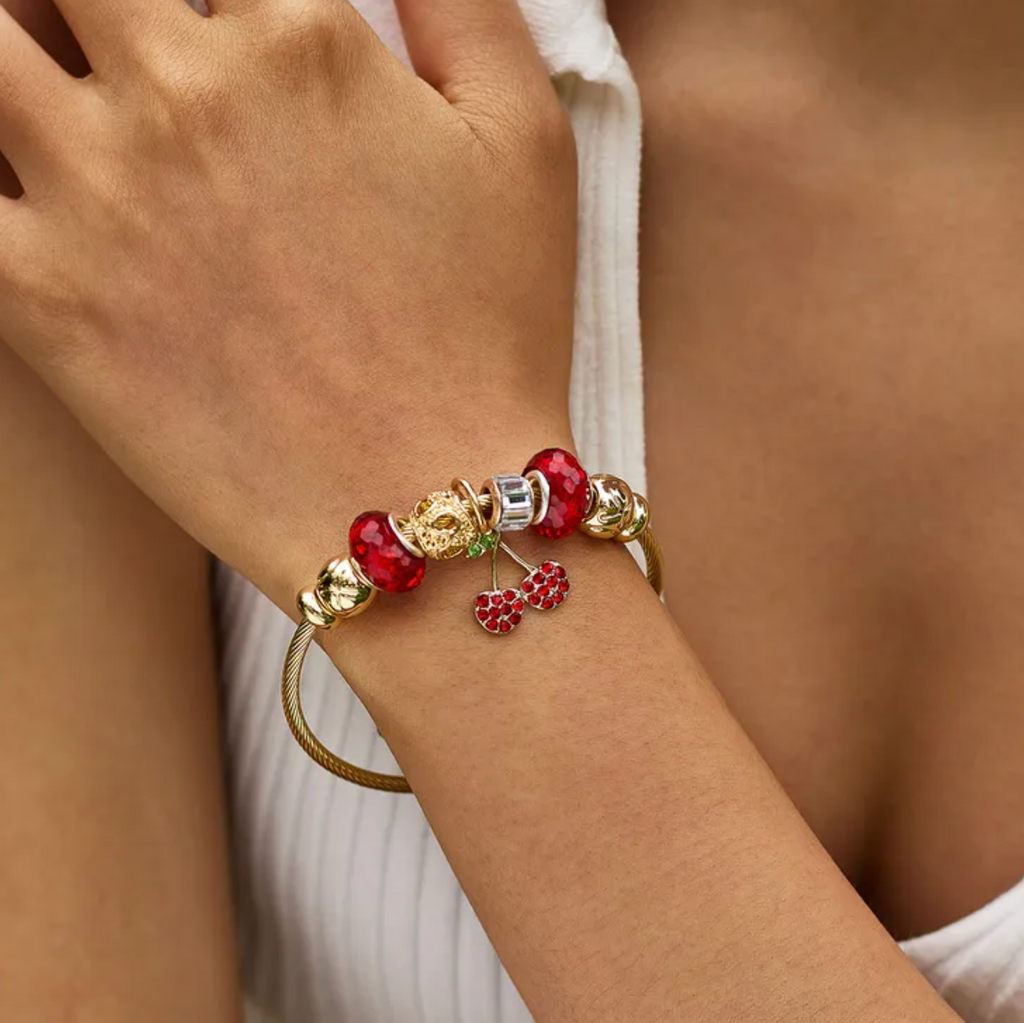 Ce bracelet rigide doré séduit par son design ludique et coloré : un ensemble de charms scintillants, dont une cerise rouge en zircon cubique, apporte éclat et originalité. Un bijou au style affirmé, parfait pour les esprits libres.

Matériaux : Acier inoxydable doré + alliage orné de zircon cubique et perles de cristal. Sans plomb, sans nickel.

Dimensions : Périmètre intérieur : 16 cm – largeur câble : 2,8 mm – poids : 20,6 g.

Style : Audacieux et vitaminé, ce bracelet s’adresse à celles qui aiment mixer