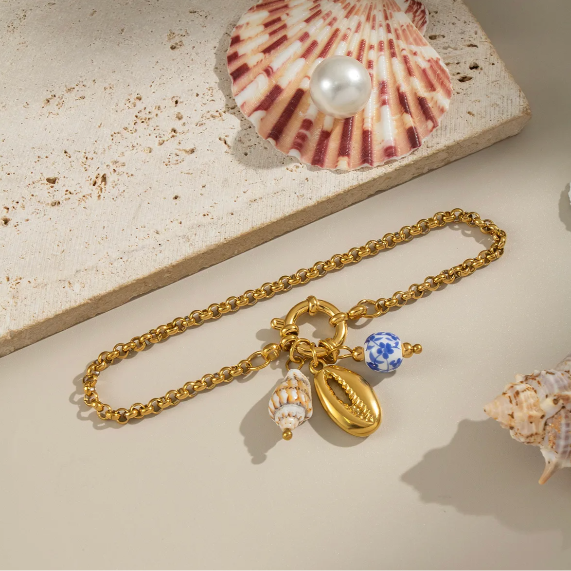 Un bracelet doré tendance, agrémenté de trois charms délicats : un cauri doré, une perle céramique bleu et blanc, et un petit coquillage naturel. Une pièce solaire et estivale, parfaite pour les tenues de bord de mer ou les looks bohèmes.

Matériau : Acier inoxydable couleur doré, hypoallergénique et résistant à l’eau. Éléments en céramique et résine.

Dimensions : Longueur 19 cm – taille des charms jusqu’à 1,8 cm – poids total 7,3 g.

Design : Maillons fins dorés à effet torsadé, fermoir anneau à bascule. 