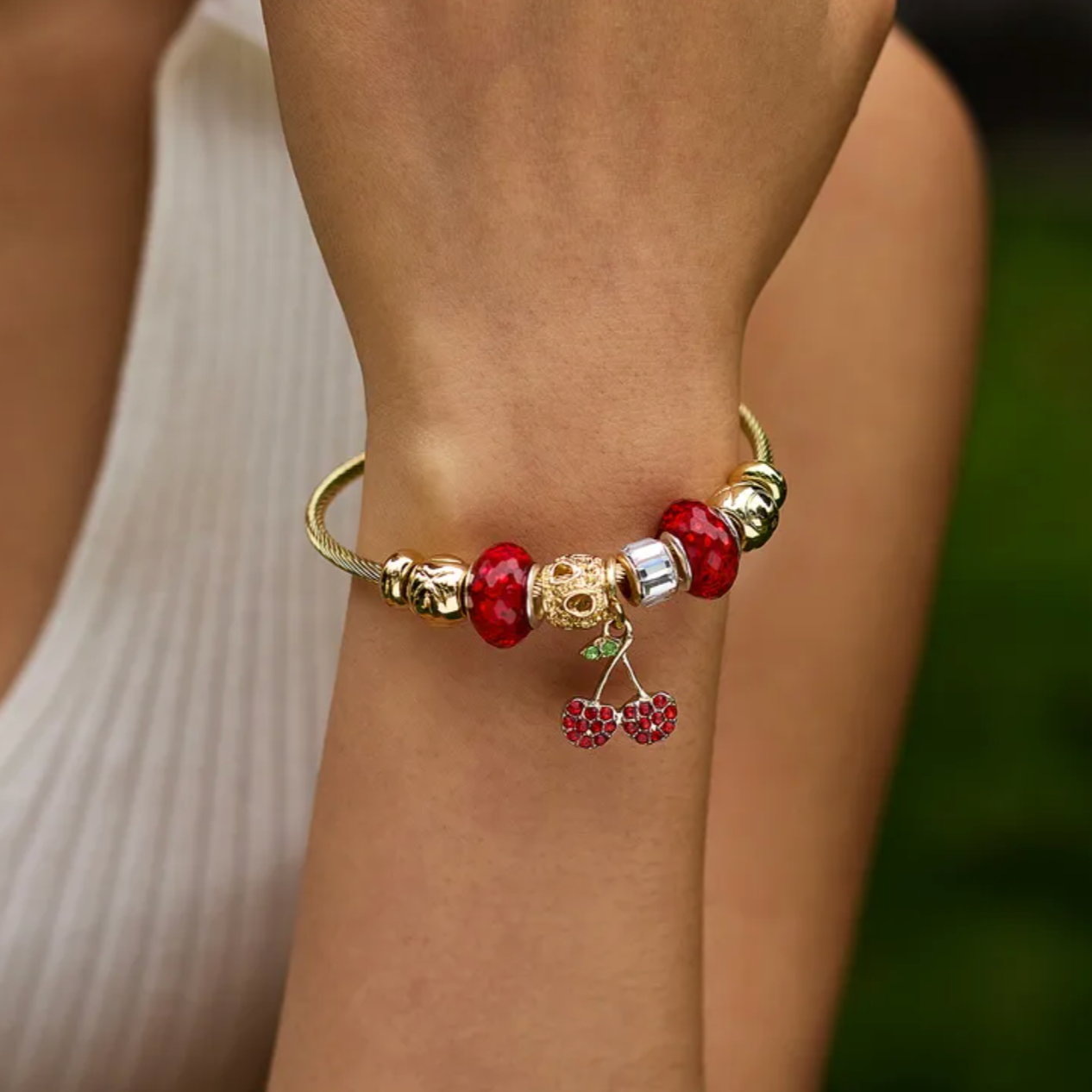 Bracelet rigide femme en acier inoxydable doré, décoré de charms scintillants dont une cerise rouge en zircon cubique et perles de cristal. Bijou fantaisie original et chic, au design coloré, audacieux et lumineux, parfait pour un look fruité et tendance