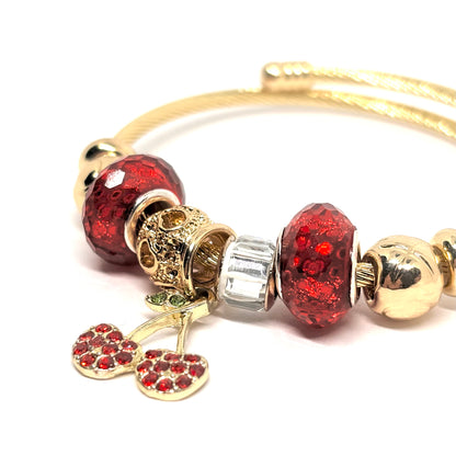 Bracelet rigide femme en acier inoxydable doré, décoré de charms scintillants dont une cerise rouge en zircon cubique et perles de cristal. Bijou fantaisie original et chic, au design coloré, audacieux et lumineux, parfait pour un look fruité et tendance