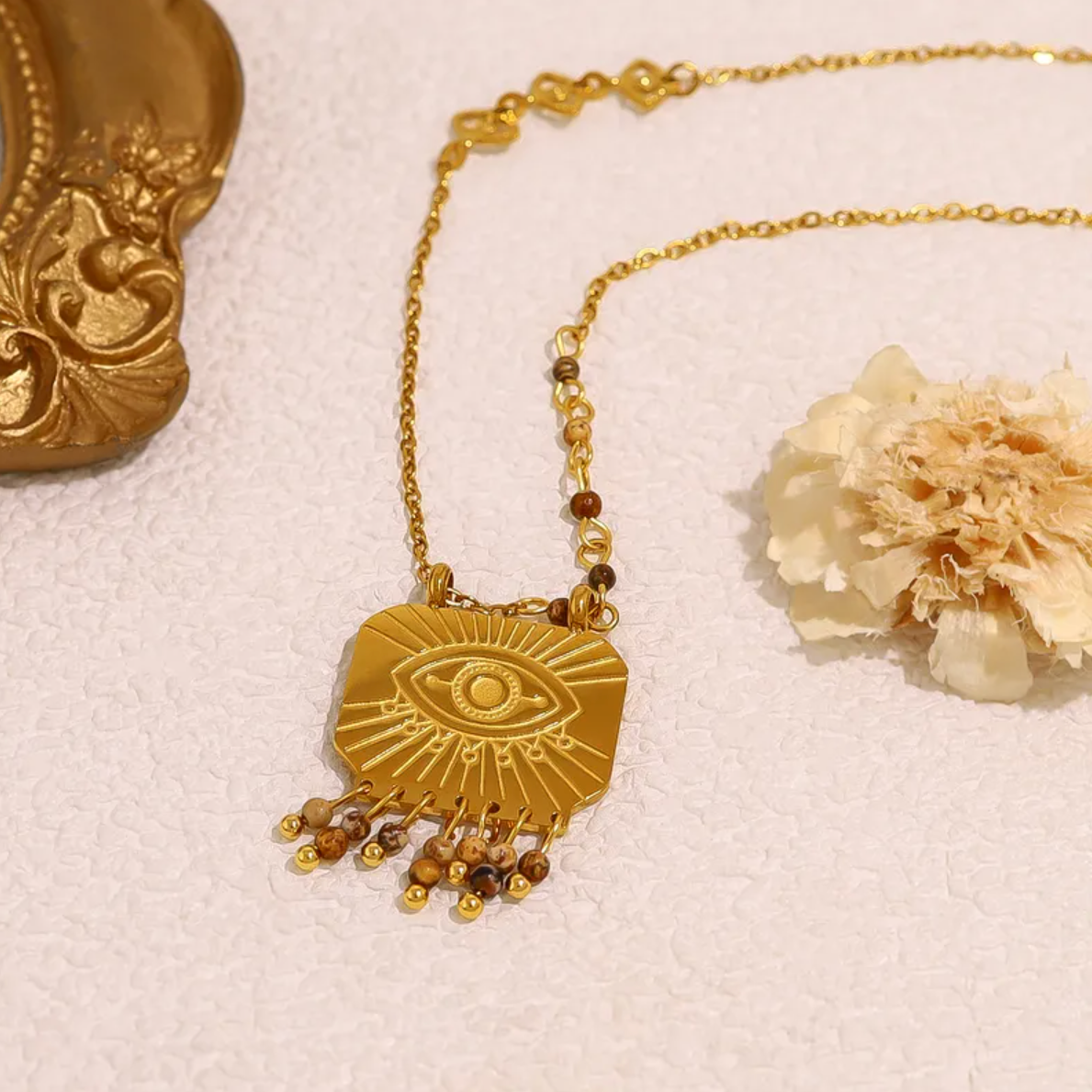 Un collier mystique et affirmé, où l’œil protecteur gravé s’entoure de détails soignés : petites pampilles en bas du pendentif et maillons décoratifs sur la chaîne. Une pièce symbolique à l’esprit bohème-chic.

Matériau : Acier inoxydable couleur doré, gravure précise, pampilles mobiles, résistant à l’eau et hypoallergénique.

Dimensions : Longueur chaîne standard avec maillons décoratifs sur le côté, pendentif carré légèrement bombé avec pampilles.

Design : Motif œil protecteur central, entouré de rayons 