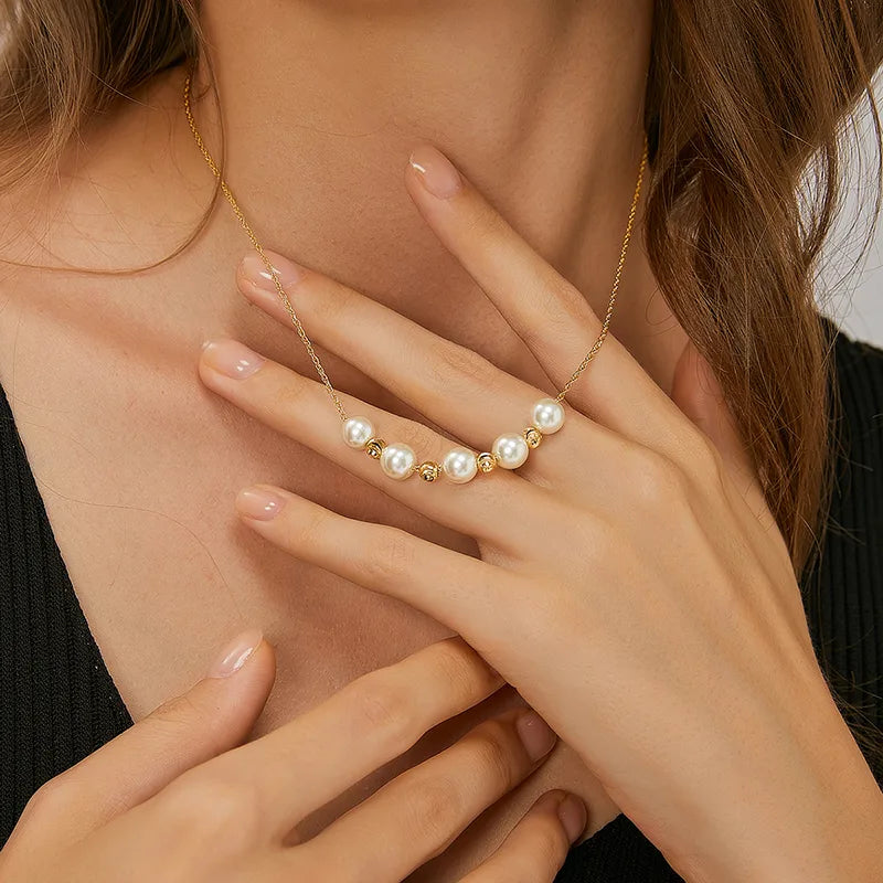 Ce collier doré conjugue élégance classique et raffinement moderne grâce à sa composition équilibrée de perles blanches nacrées et de boules dorées rainurées. Disposées en demi-cercle au centre d’une chaîne torsadée couleur or, les perles captent délicatement la lumière et apportent une touche de lumière soyeuse au décolleté.
