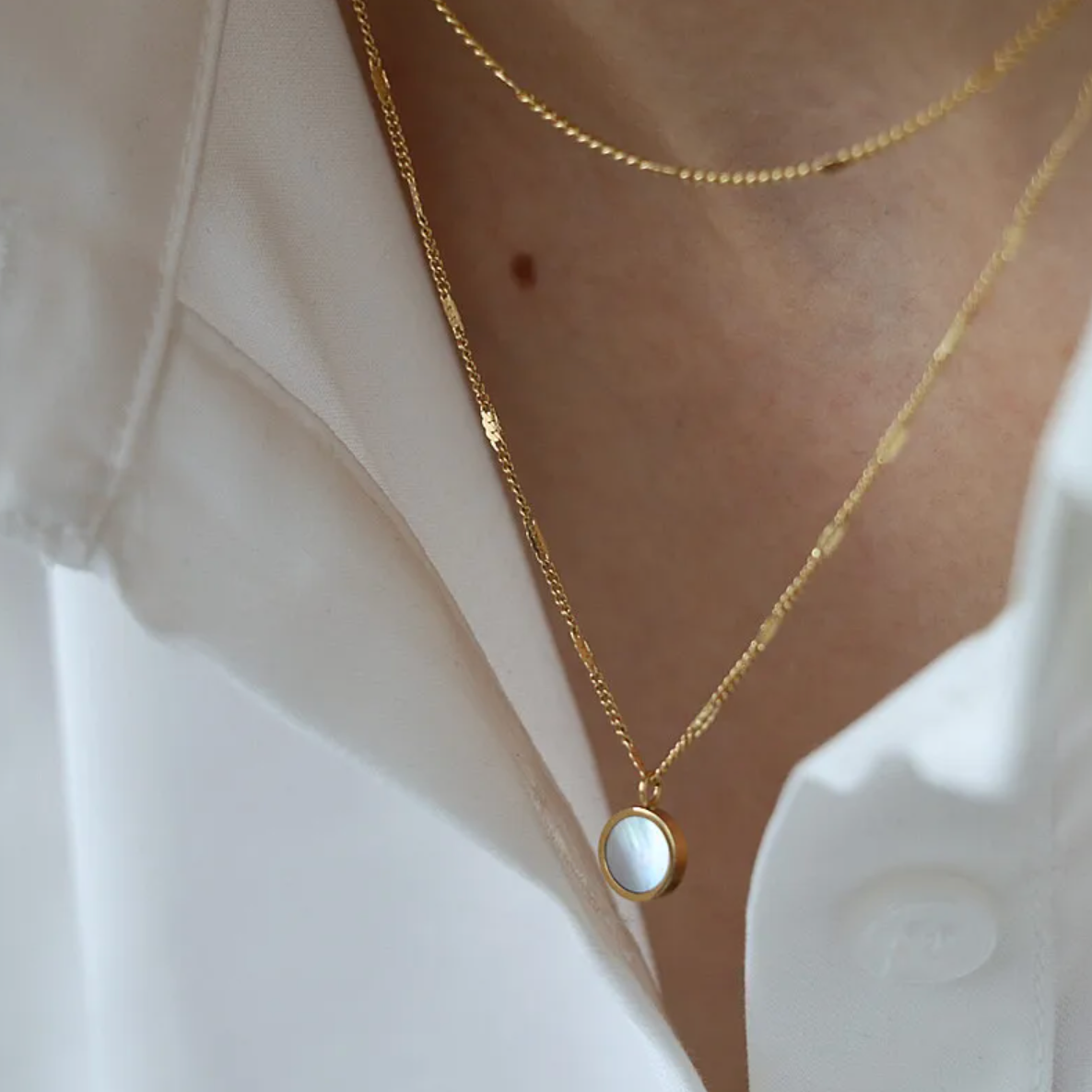 Un collier fin et délicat à double chaîne dorée, rehaussé d’un médaillon rond en nacre naturelle, pour une touche à la fois lumineuse et poétique. Ce bijou joue sur les superpositions tout en conservant une allure épurée.

Matériau : Acier inoxydable couleur doré, résistant à l’eau, hypoallergénique. Insert de nacre naturelle pour une brillance subtile.

Dimensions : Deux chaînes de longueurs différentes formant un effet superposé. Médaillon : diamètre approx. 12 mm.

Design : Mailles fines ponctuées de per