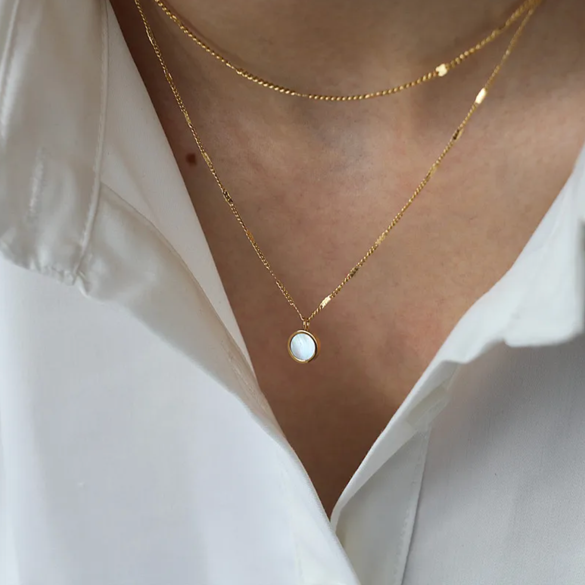 Un collier fin et délicat à double chaîne dorée, rehaussé d’un médaillon rond en nacre naturelle, pour une touche à la fois lumineuse et poétique. Ce bijou joue sur les superpositions tout en conservant une allure épurée.

Matériau : Acier inoxydable couleur doré, résistant à l’eau, hypoallergénique. Insert de nacre naturelle pour une brillance subtile.

Dimensions : Deux chaînes de longueurs différentes formant un effet superposé. Médaillon : diamètre approx. 12 mm.

Design : Mailles fines ponctuées de per