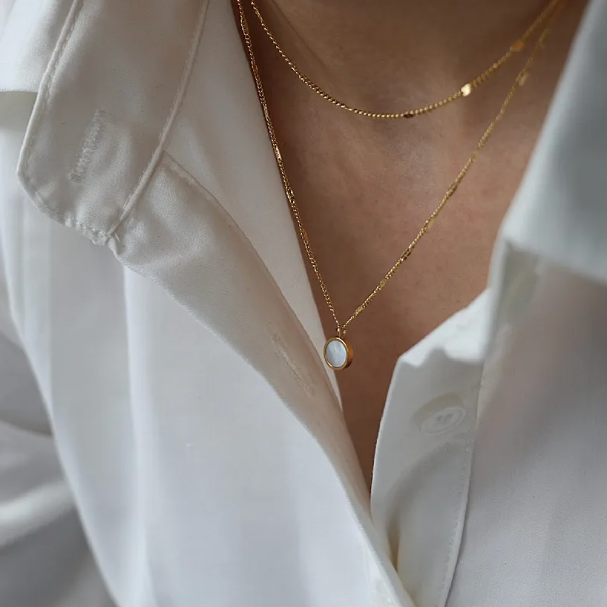 Un collier fin et délicat à double chaîne dorée, rehaussé d’un médaillon rond en nacre naturelle, pour une touche à la fois lumineuse et poétique. Ce bijou joue sur les superpositions tout en conservant une allure épurée.

Matériau : Acier inoxydable couleur doré, résistant à l’eau, hypoallergénique. Insert de nacre naturelle pour une brillance subtile.

Dimensions : Deux chaînes de longueurs différentes formant un effet superposé. Médaillon : diamètre approx. 12 mm.

Design : Mailles fines ponctuées de per
