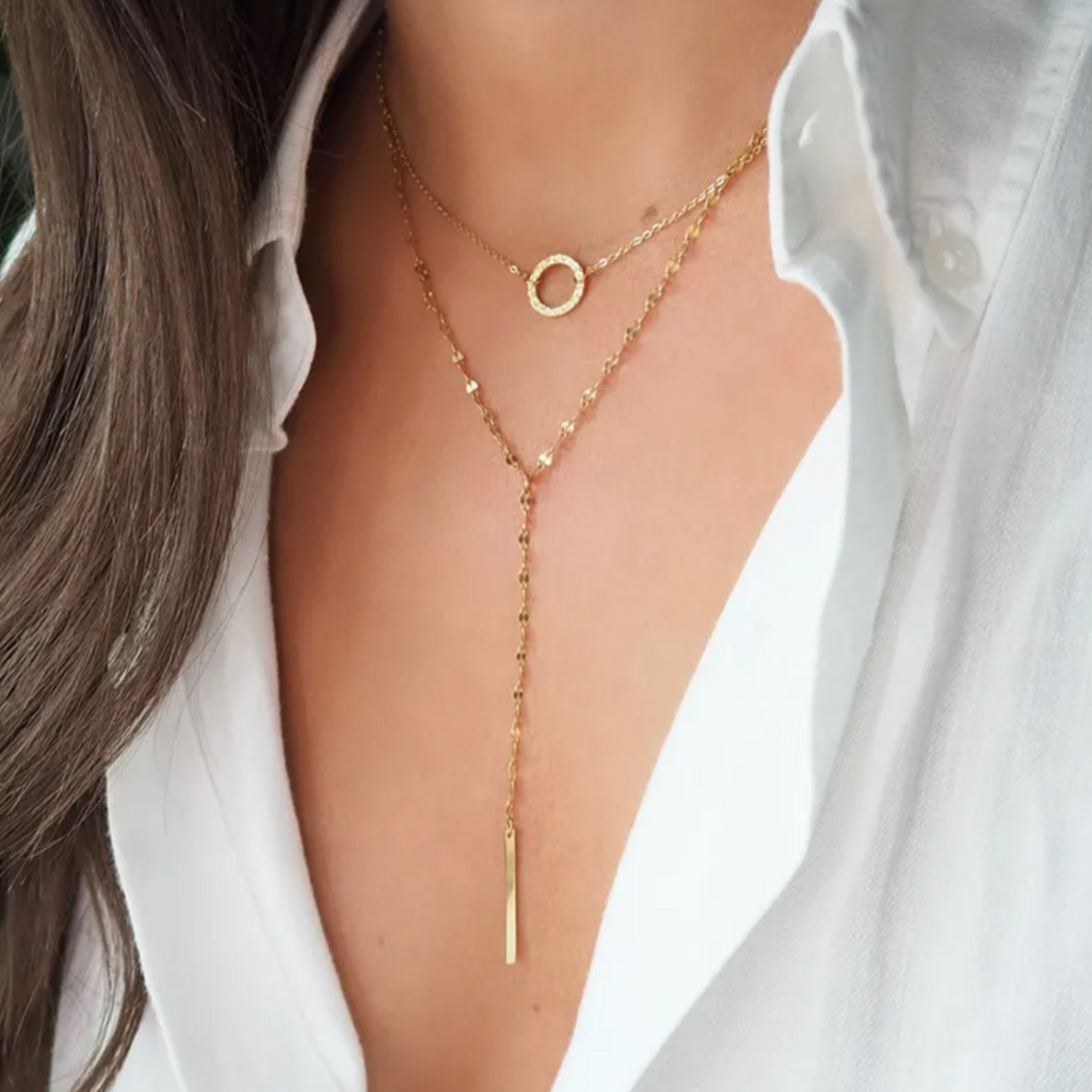 Un collier double rang à la silhouette élancée et épurée, qui joue sur les lignes graphiques et les volumes délicats. Le médaillon circulaire et la barre verticale s’équilibrent avec élégance pour une allure minimaliste et sophistiquée.

Matériau : Acier inoxydable couleur doré, finition brillante, résistant à l’eau, hypoallergénique.

Dimensions : Longueur totale env. 45 cm + extension – pendentif barre env. 5 cm de chute verticale. Léger et confortable au porté.

Design : Deux chaînes fines superposées : 