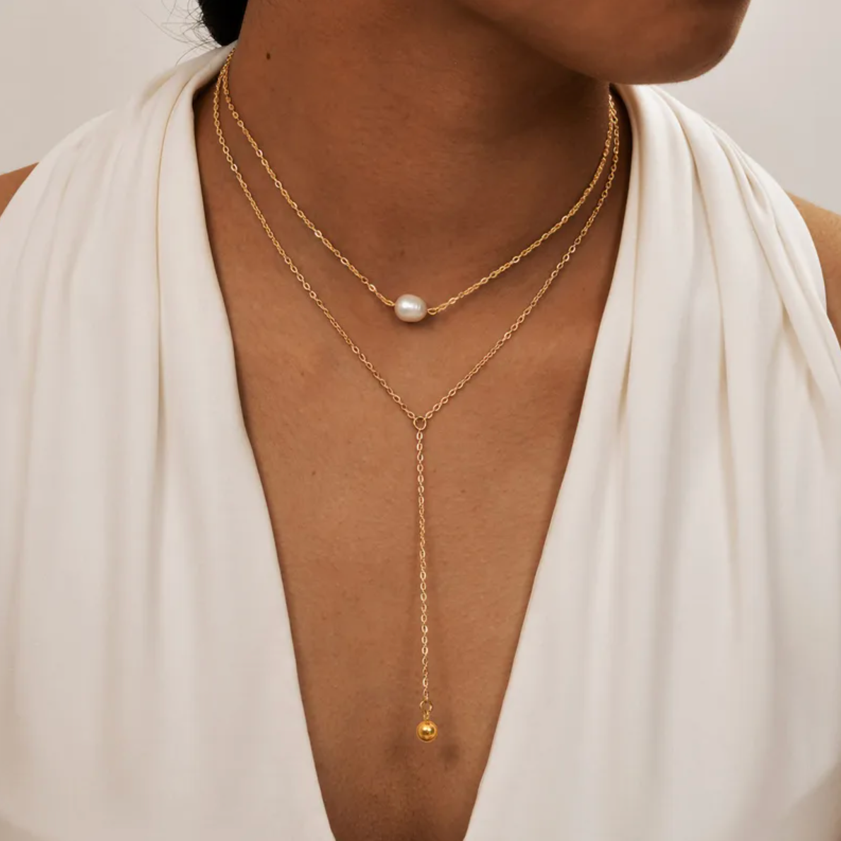 Ce collier double rang en acier inoxydable doré, orné d'une perle blanche nacrée et d'une chaînette tombante, crée un effet chic et structuré. Un bijou à la fois moderne et sophistiqué, idéal pour sublimer un décolleté.

Matériau : Acier inoxydable couleur doré, placage PVD or 18K, perle synthétique (effet nacré), hypoallergénique, résistant à l’eau et à l’oxydation.