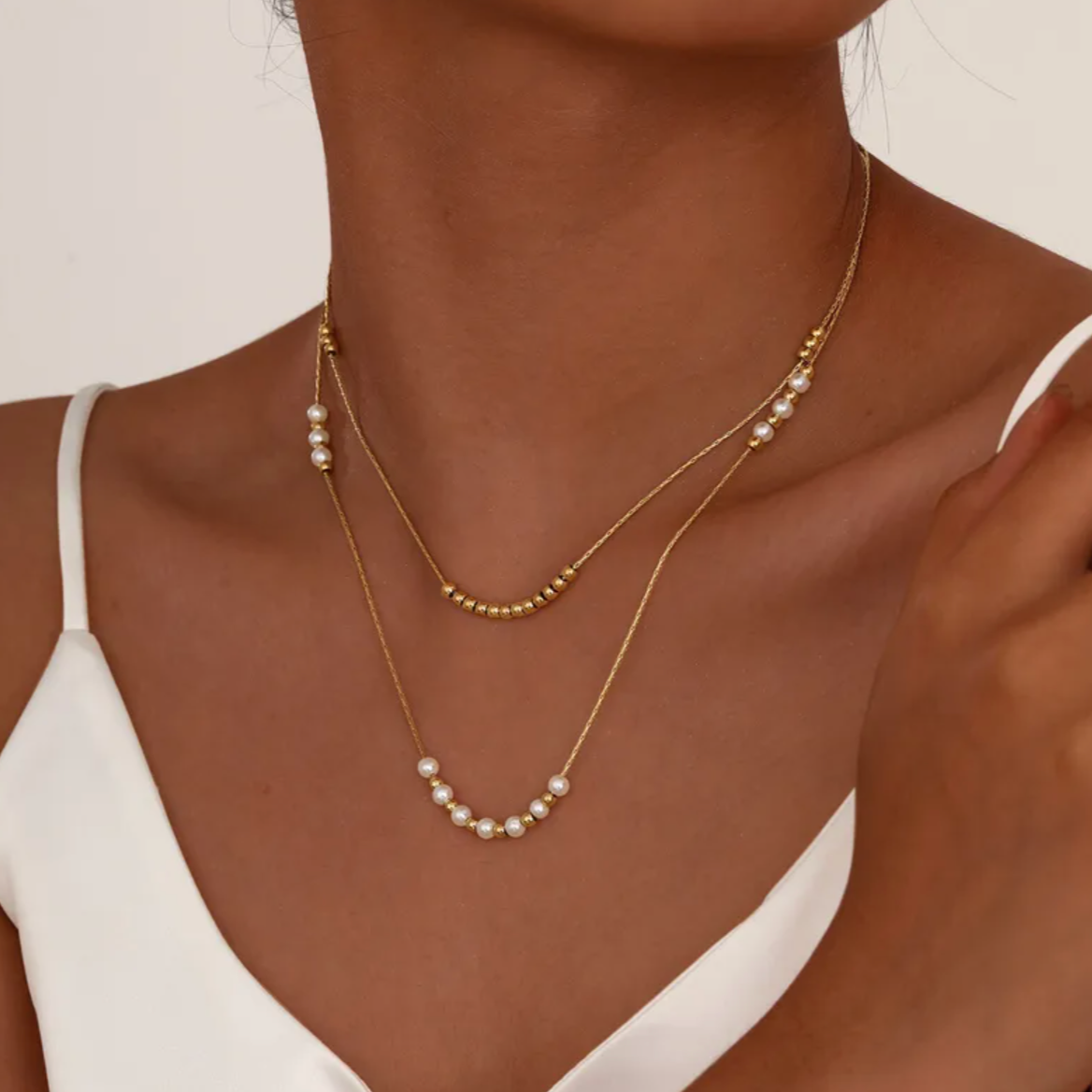 Collier double rang pour femme en acier inoxydable couleur doré, orné de perles blanches nacrées et de petites billes dorées. Bijou raffiné et lumineux, résistant à l’eau, au design délicat et minimaliste idéal pour un style chic et féminin