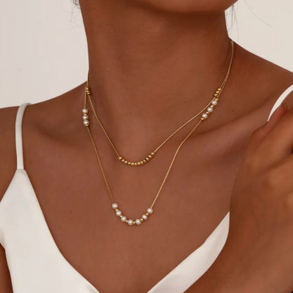 Collier double rang pour femme en acier inoxydable couleur doré, orné de perles blanches nacrées et de petites billes dorées. Bijou raffiné et lumineux, résistant à l’eau, au design délicat et minimaliste idéal pour un style chic et féminin