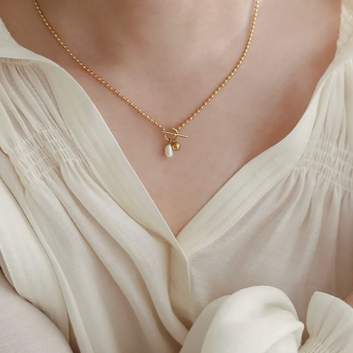 collier femme en acier inoxydable doré 14K avec fermoir toggle apparent, orné d’une perle blanche irrégulière et d’une perle dorée brillante, longueur 45 cm, bijou minimaliste et raffiné au style moderne