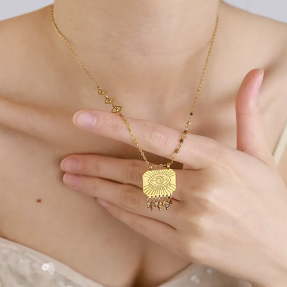 collier femme en acier inoxydable doré avec pendentif carré gravé d’un œil protecteur entouré de pampilles et maillons décoratifs, bijou talisman au style bohème chic et symbolique