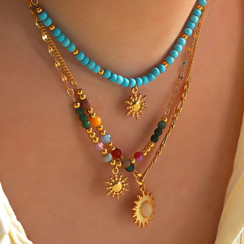 collier femme en acier inoxydable doré avec pendentif soleil à rayons texturés et chaîne asymétrique mêlant maillons plats et perles multicolores, bijou bohème et lumineux à offrir