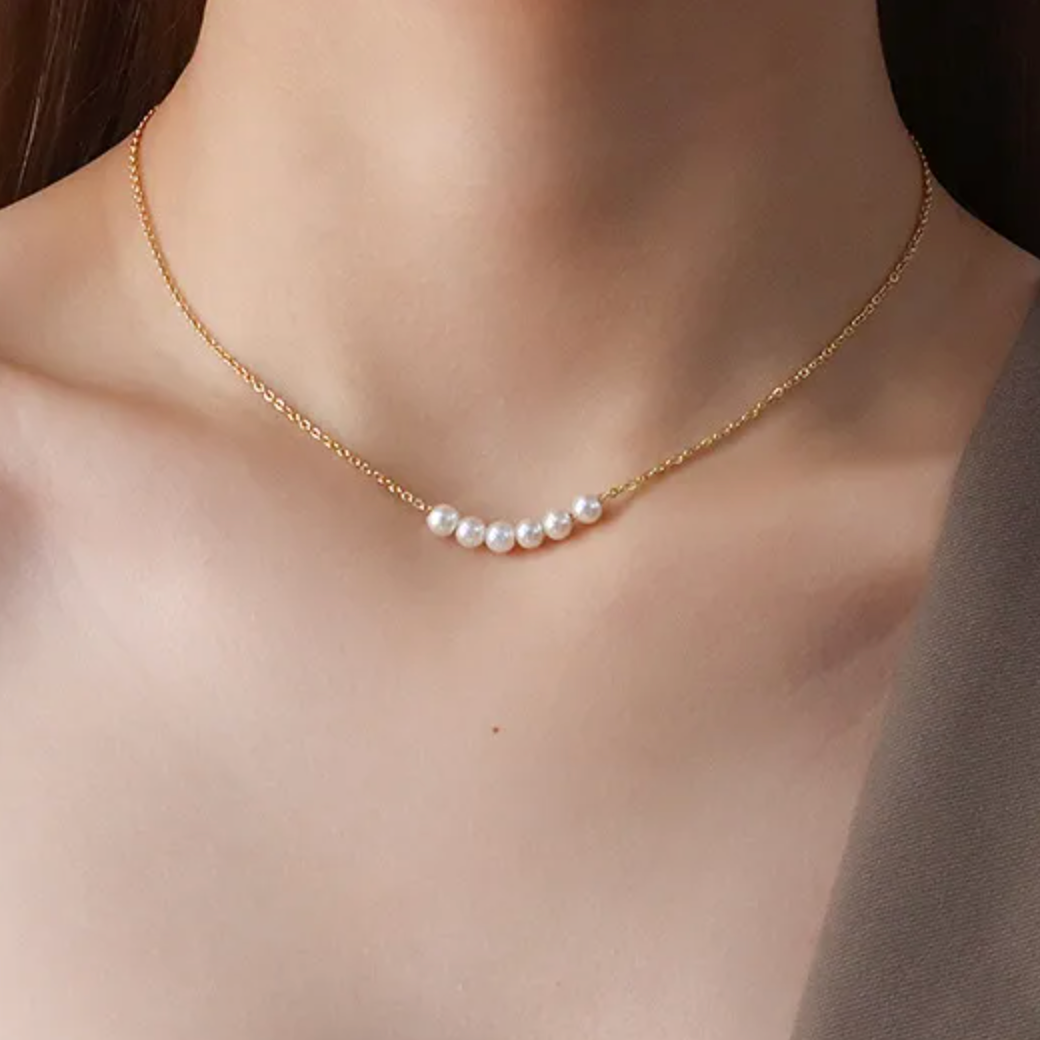 Collier pour femme en acier inoxydable couleur doré, orné de sept perles blanches nacrées alignées au centre. Bijou minimaliste et raffiné, résistant à l’eau, idéal pour un style chic et intemporel au quotidien.