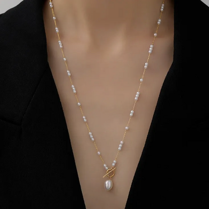 Collier doré pour femme en acier inoxydable, orné de perles blanches et d’un pendentif perle baroque suspendu à un fermoir toggle décoratif. Bijou raffiné, résistant à l’eau, au style chic et romantique idéal pour une tenue élégante ou bohème