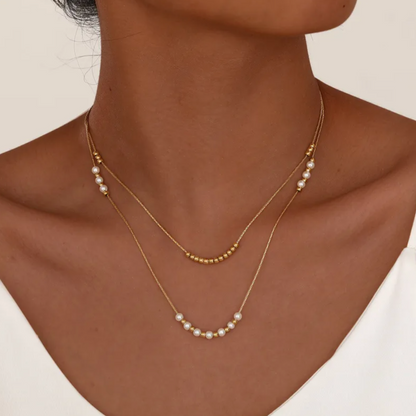 Collier double rang pour femme en acier inoxydable couleur doré, orné de perles blanches nacrées et de petites billes dorées. Bijou raffiné et lumineux, résistant à l’eau, au design délicat et minimaliste idéal pour un style chic et féminin