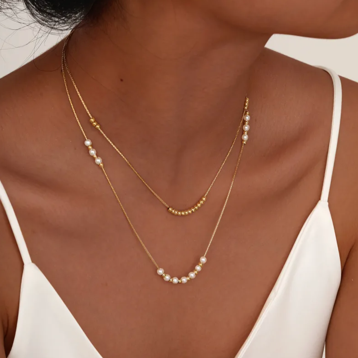 Collier double rang pour femme en acier inoxydable couleur doré, orné de perles blanches nacrées et de petites billes dorées. Bijou raffiné et lumineux, résistant à l’eau, au design délicat et minimaliste idéal pour un style chic et féminin