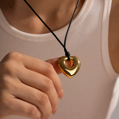 Collier long pour femme avec pendentif cœur doré en acier inoxydable suspendu à un cordon noir. Bijou moderne et graphique, au design massif et miroir, idéal pour un look audacieux et contemporain
