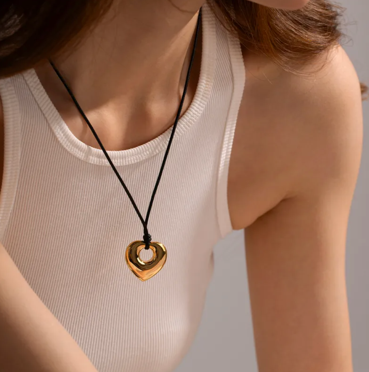 Collier long pour femme avec pendentif cœur doré en acier inoxydable suspendu à un cordon noir. Bijou moderne et graphique, au design massif et miroir, idéal pour un look audacieux et contemporain