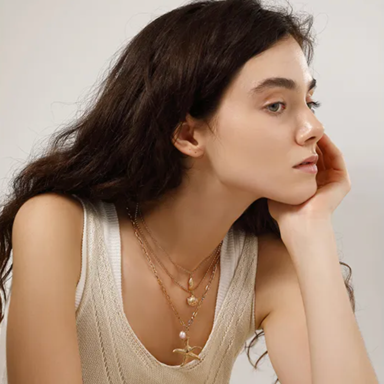 Collier multi-rangs pour femme en acier inoxydable couleur doré, orné de pendentifs coquillage, étoile de mer et perle nacrée. Bijou lumineux et estival au style bohème et marin, parfait pour un look vacances chic