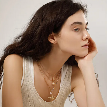 Collier multi-rangs pour femme en acier inoxydable couleur doré, orné de pendentifs coquillage, étoile de mer et perle nacrée. Bijou lumineux et estival au style bohème et marin, parfait pour un look vacances chic