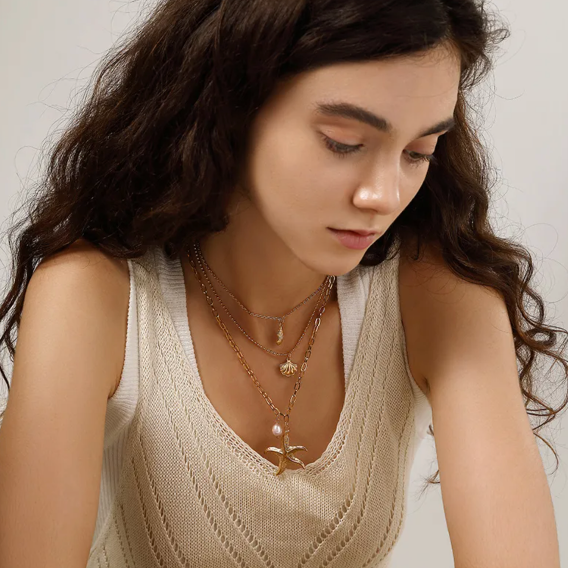 Collier multi-rangs pour femme en acier inoxydable couleur doré, orné de pendentifs coquillage, étoile de mer et perle nacrée. Bijou lumineux et estival au style bohème et marin, parfait pour un look vacances chic