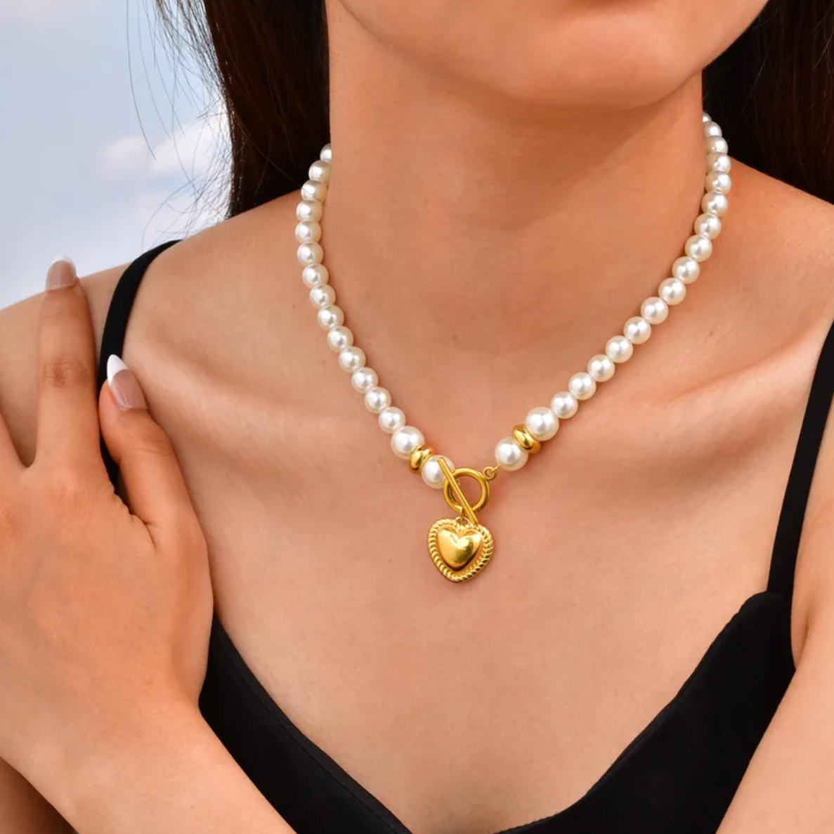 Collier pour femme composé de perles blanches nacrées et de perles dorées, orné d’un pendentif cœur bombé couleur or avec fermoir toggle à l’avant. Bijou romantique et vintage en acier inoxydable, résistant à l’eau et hypoallergénique.
