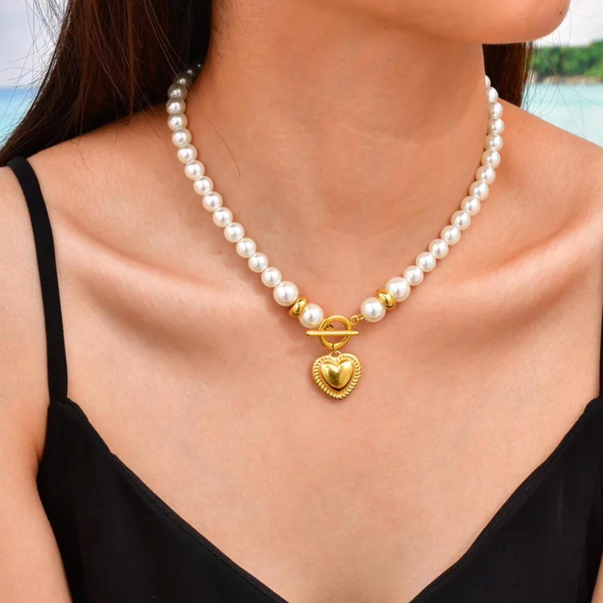 Collier pour femme composé de perles blanches nacrées et de perles dorées, orné d’un pendentif cœur bombé couleur or avec fermoir toggle à l’avant. Bijou romantique et vintage en acier inoxydable, résistant à l’eau et hypoallergénique.