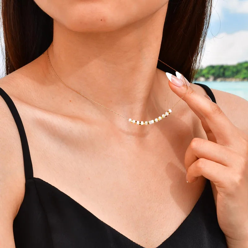 Ce collier minimaliste allie élégance intemporelle et style décontracté chic. Il se compose d’une fine chaîne couleur or ornée de perles plates blanches et dorées, disposées en alternance pour créer un rythme visuel doux et équilibré. Le contraste subtil entre la nacre blanche et le doré lumineux en fait un bijou délicat, parfait pour illuminer le décolleté avec discrétion.