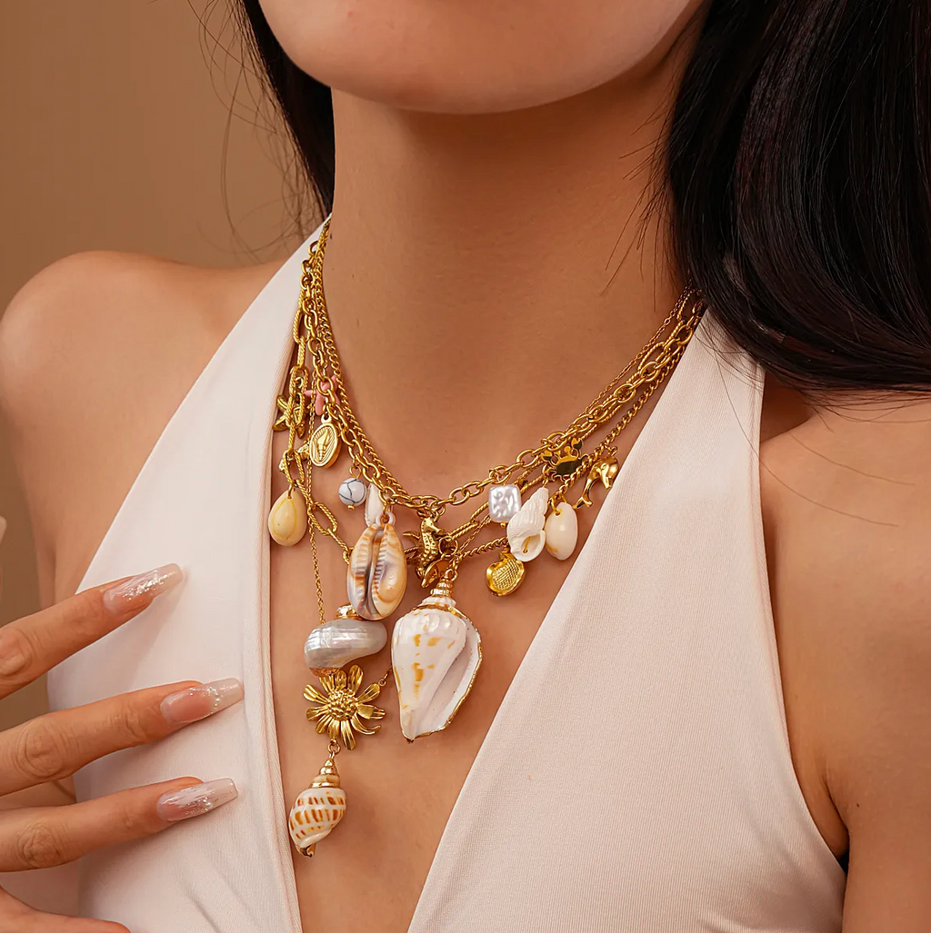 Un collier solaire et organique, associant une fleur dorée texturée à un véritable coquillage, pour un look bohème chic aux accents marins.

Matériau : Acier titane couleur doré, coquillage naturel – hypoallergénique et résistant à l’eau.

Dimensions : Longueur totale 49,5 cm + chaîne d’extension 8 cm – poids léger : 6,5 g.

Design : La fleur centrale aux pétales sculptés sert de base à un coquillage suspendu, apportant un effet organique et raffiné. Finition soignée.

Style : Parfait pour l’été, les tenues