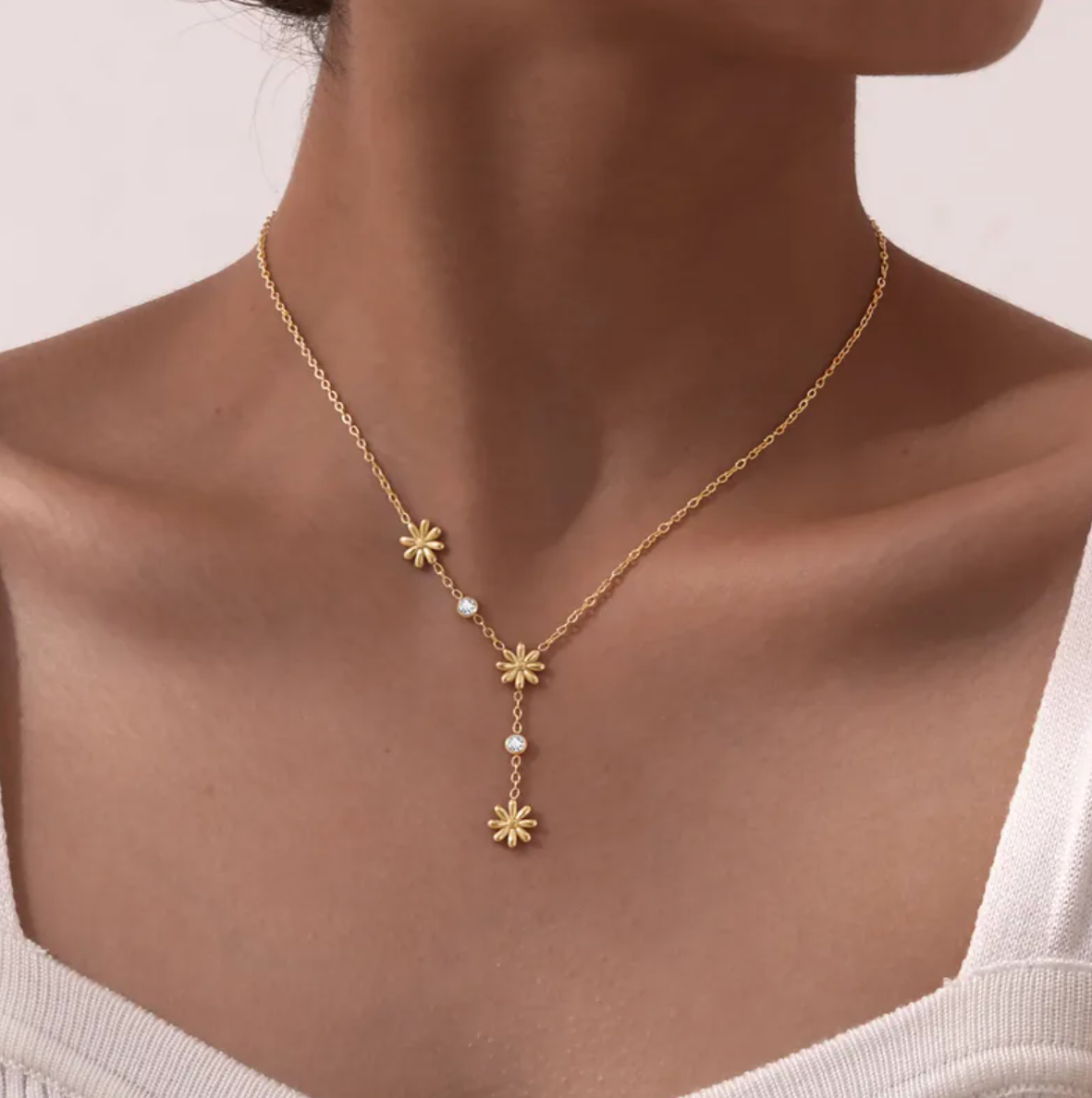 Un collier délicat et graphique, jouant sur une asymétrie florale et des cristaux étincelants. Parfait pour apporter une touche de lumière à un look sobre ou romantique.

Matériau : Acier inoxydable couleur doré, orné de cristaux transparents – résistant à l’eau, hypoallergénique.

Dimensions : Longueur ajustable 40 à 45 cm – pendentifs fleurs : 0,9 cm – poids léger : 4 g.

Design : Trois petites fleurs dorées disposées de façon décalée, reliées par une fine chaîne ponctuée de pierres brillantes. Un jeu de 