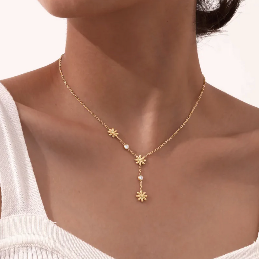 Un collier délicat et graphique, jouant sur une asymétrie florale et des cristaux étincelants. Parfait pour apporter une touche de lumière à un look sobre ou romantique.

Matériau : Acier inoxydable couleur doré, orné de cristaux transparents – résistant à l’eau, hypoallergénique.

Dimensions : Longueur ajustable 40 à 45 cm – pendentifs fleurs : 0,9 cm – poids léger : 4 g.

Design : Trois petites fleurs dorées disposées de façon décalée, reliées par une fine chaîne ponctuée de pierres brillantes. Un jeu de 